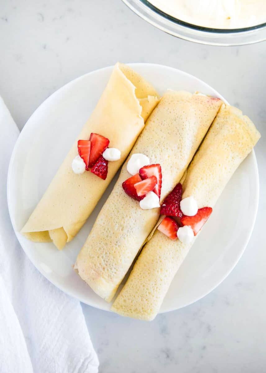 Rolled crepes with strawberries and cream on top.