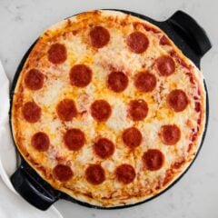 No yeast pizza dough topped with cheese and pepperoni on pizza stone.