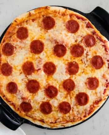 No yeast pizza dough topped with cheese and pepperoni on pizza stone.