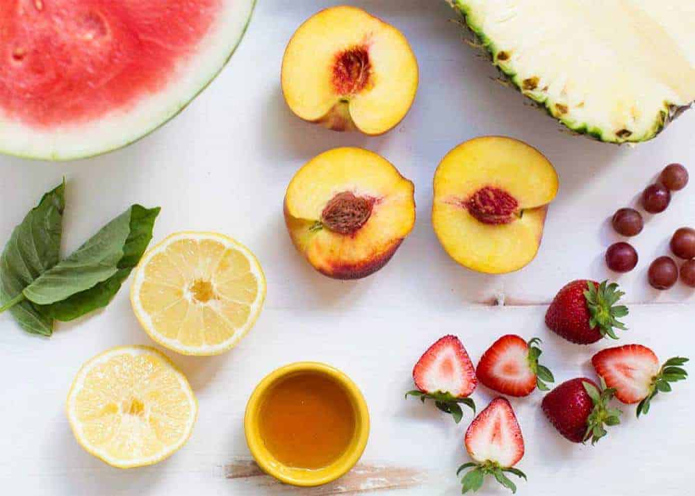 Fresh fruit and a small bowl of honey sitting on counter.