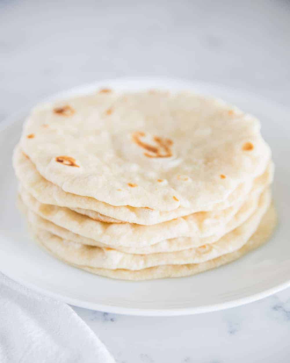 Stack of homemade flour tortillas on a white plate.
