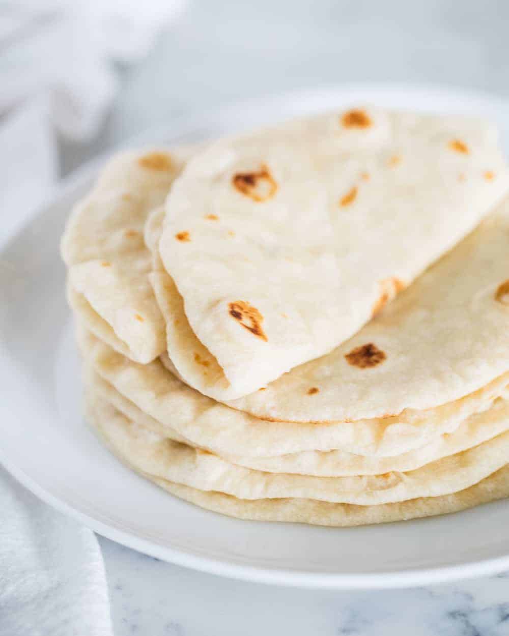 Stack of homemade flour tortillas with the top one folded in half.