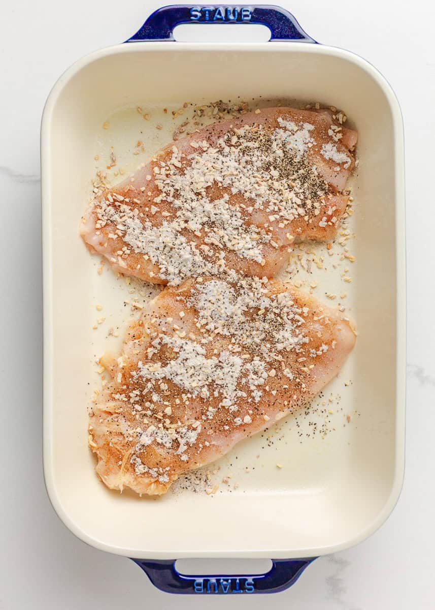 Chicken breasts seasoned with onion soup mix, salt and pepper in a baking dish.
