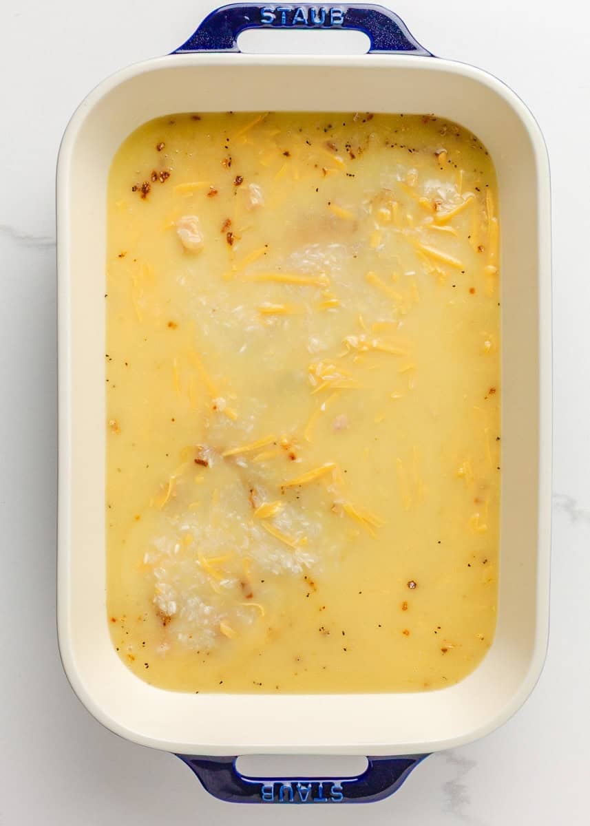 Uncooked chicken and rice casserole in a baking dish, covered with broth and cream sauce.