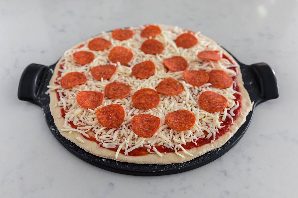 Unbaked no yeast pizza dough topped with sauce, mozzarella and pepperoni on a black pizza pan.