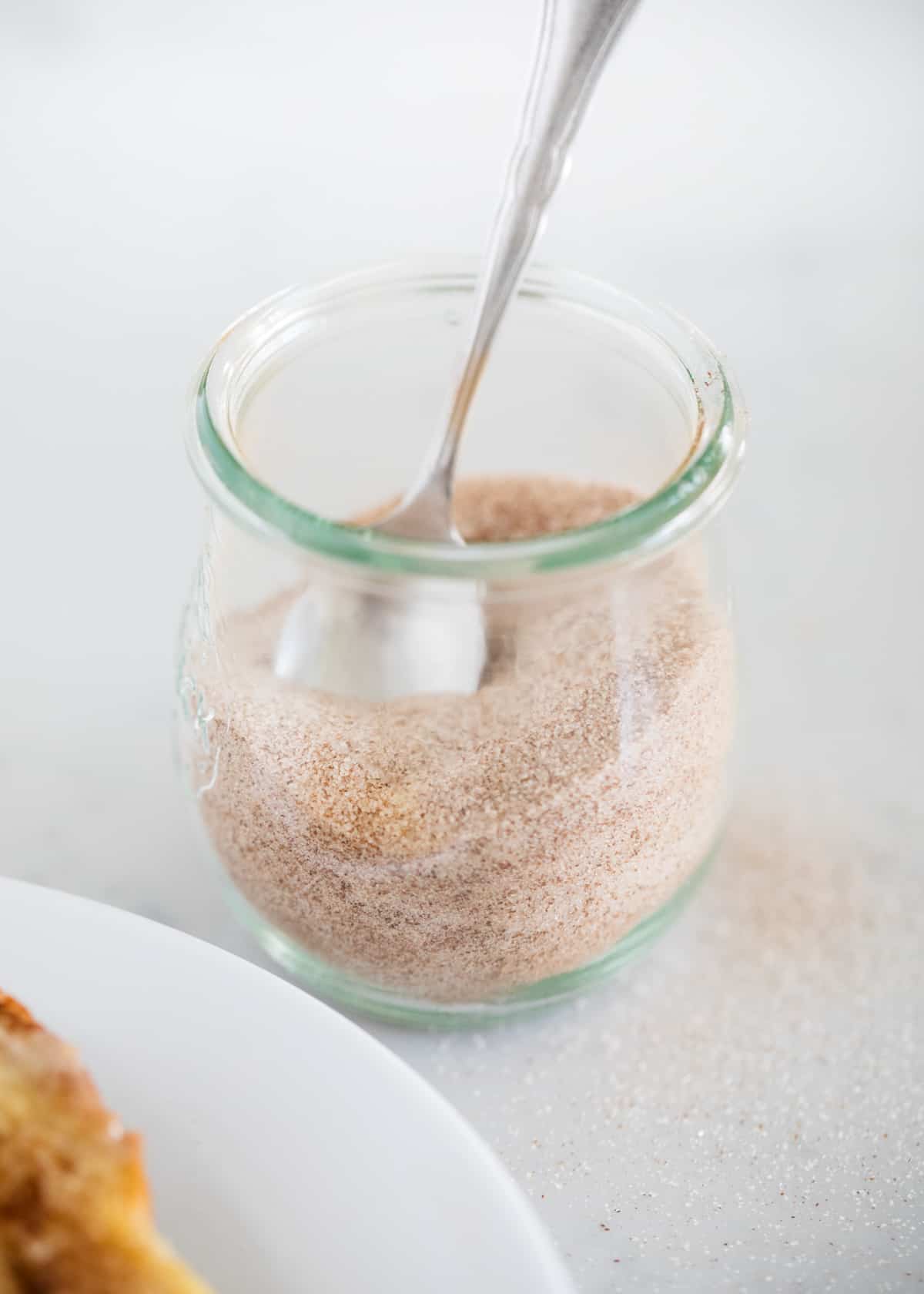 Cinnamon sugar in a glass jar with spoon.