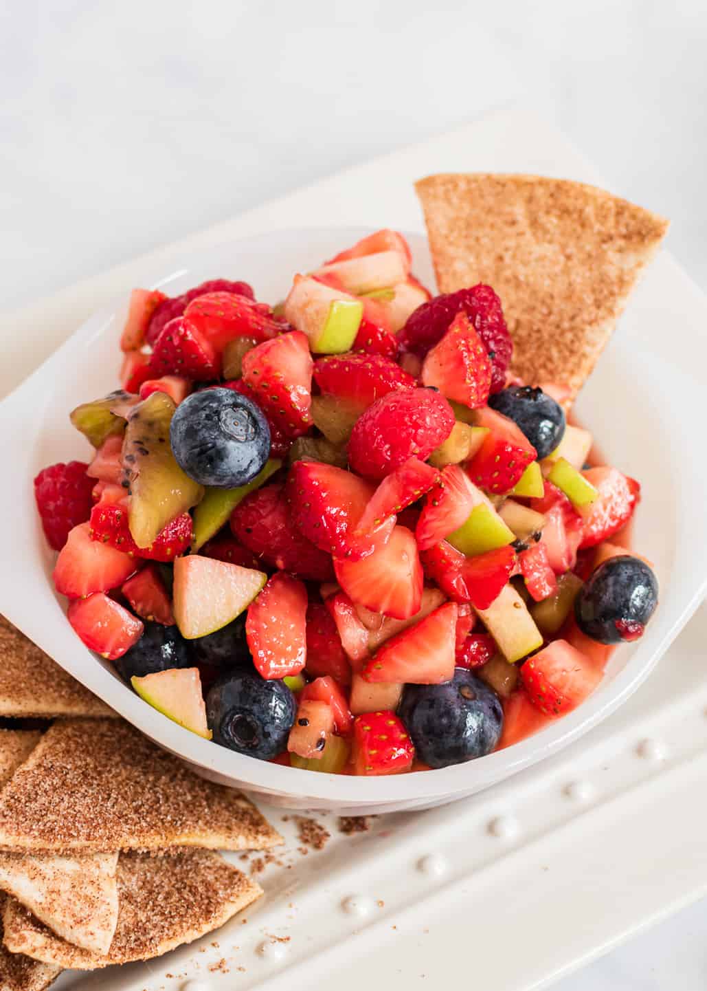 Fruit salsa in white bowl with cinnamon chips.