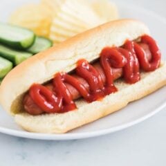 Showing a boiled hot dog on a bun with ketchup.