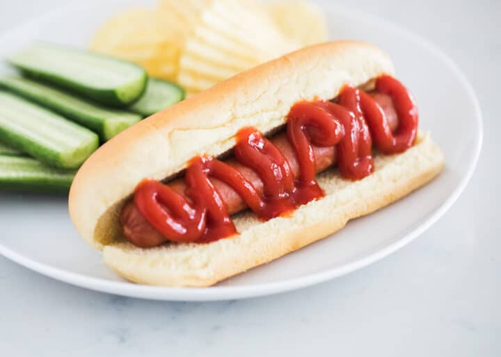 hot dog on white plate with ketchup