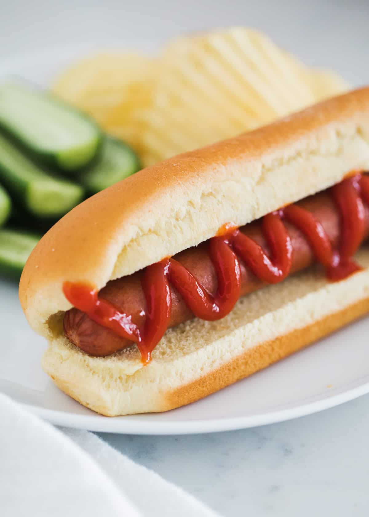 Hot dog with ketchup on white plate.