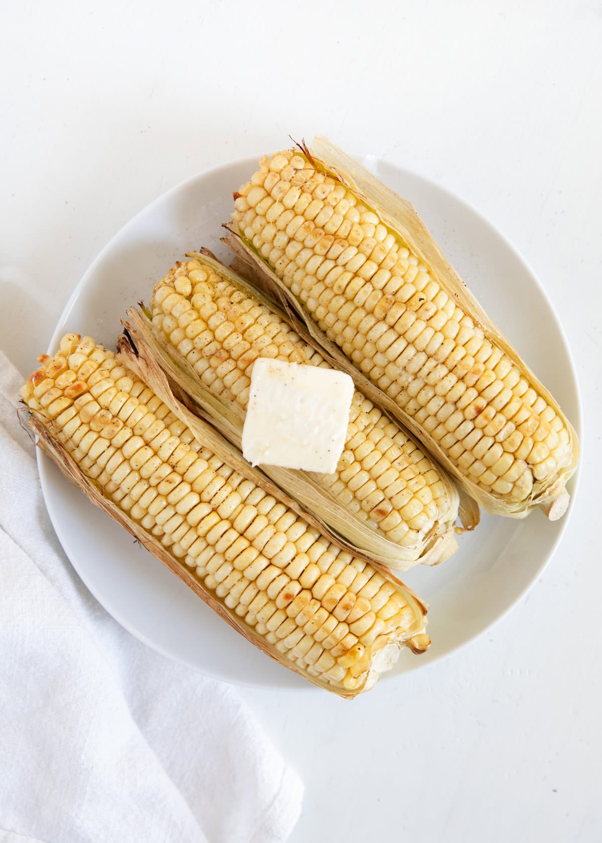 Grilled corn on the cob on a plate with a pat of butter.