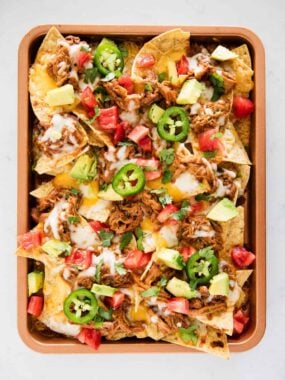 BBQ nachos with pulled pork, cheese and fresh toppings on a sheet pan.