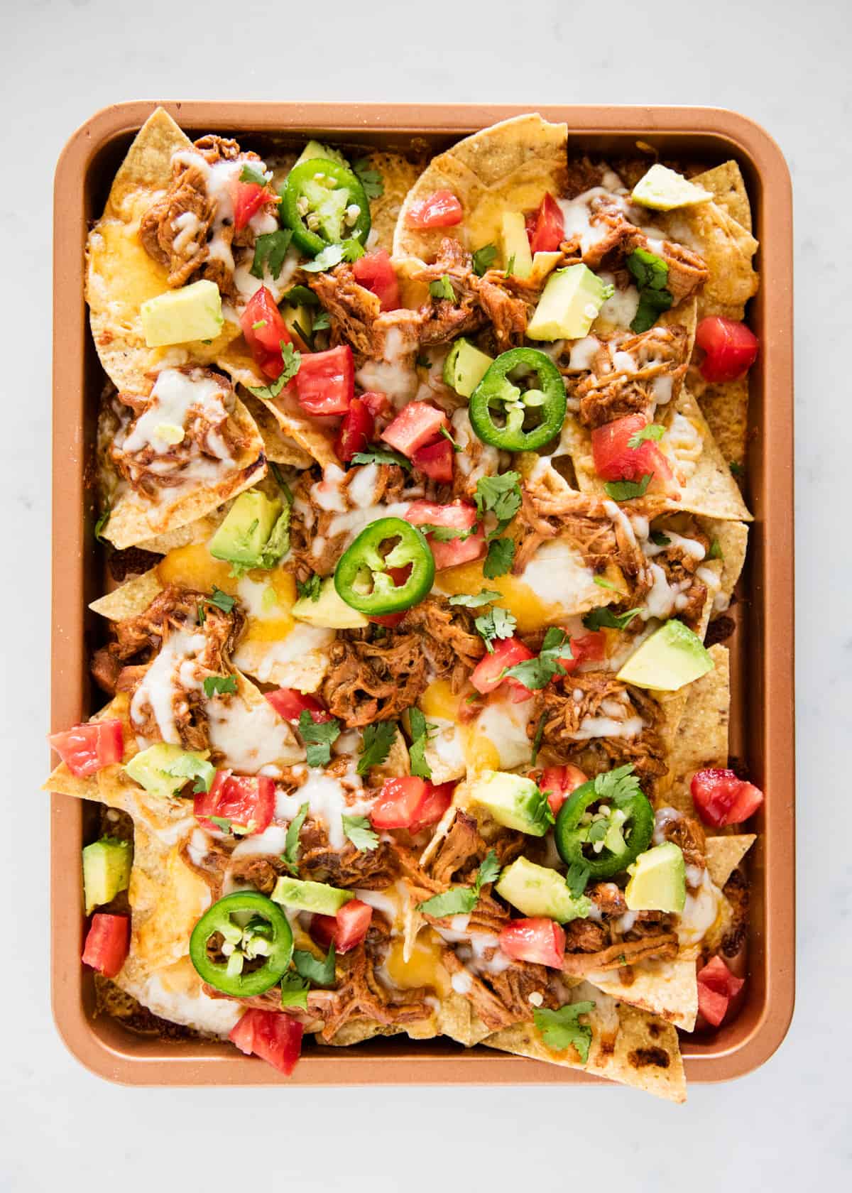 Bbq pork nachos on a sheet pan with toppings on top.