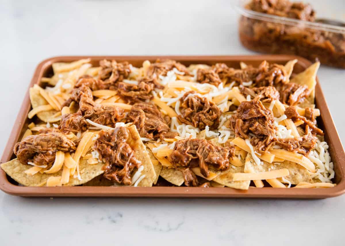 Placing bbq pork on tortilla chips with cheese.