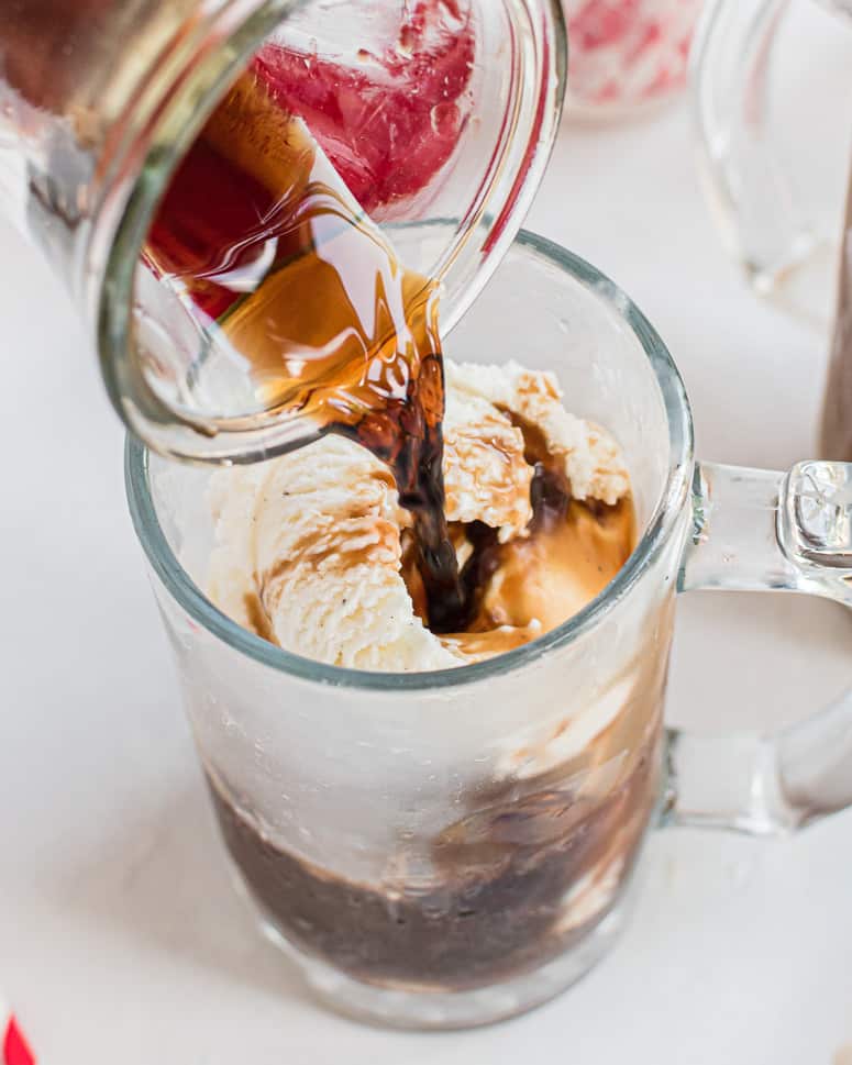 Pouring root beer over ice cream in glass.