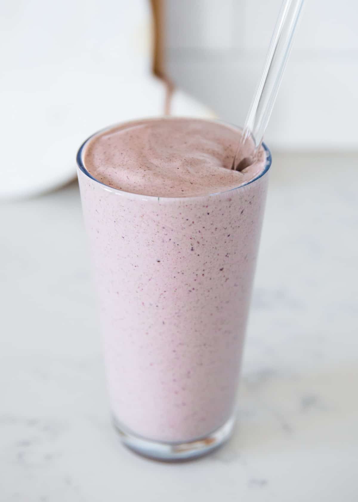 Berry protein smoothie in a glass cup with a straw.