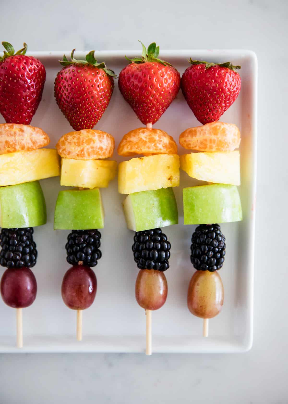 Rainbow fruit kabobs on a white plate.