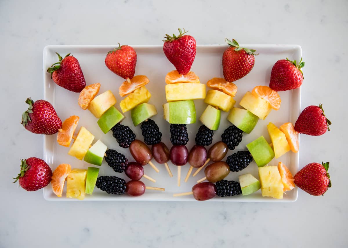 Rainbow fruit kabobs on a white plate.