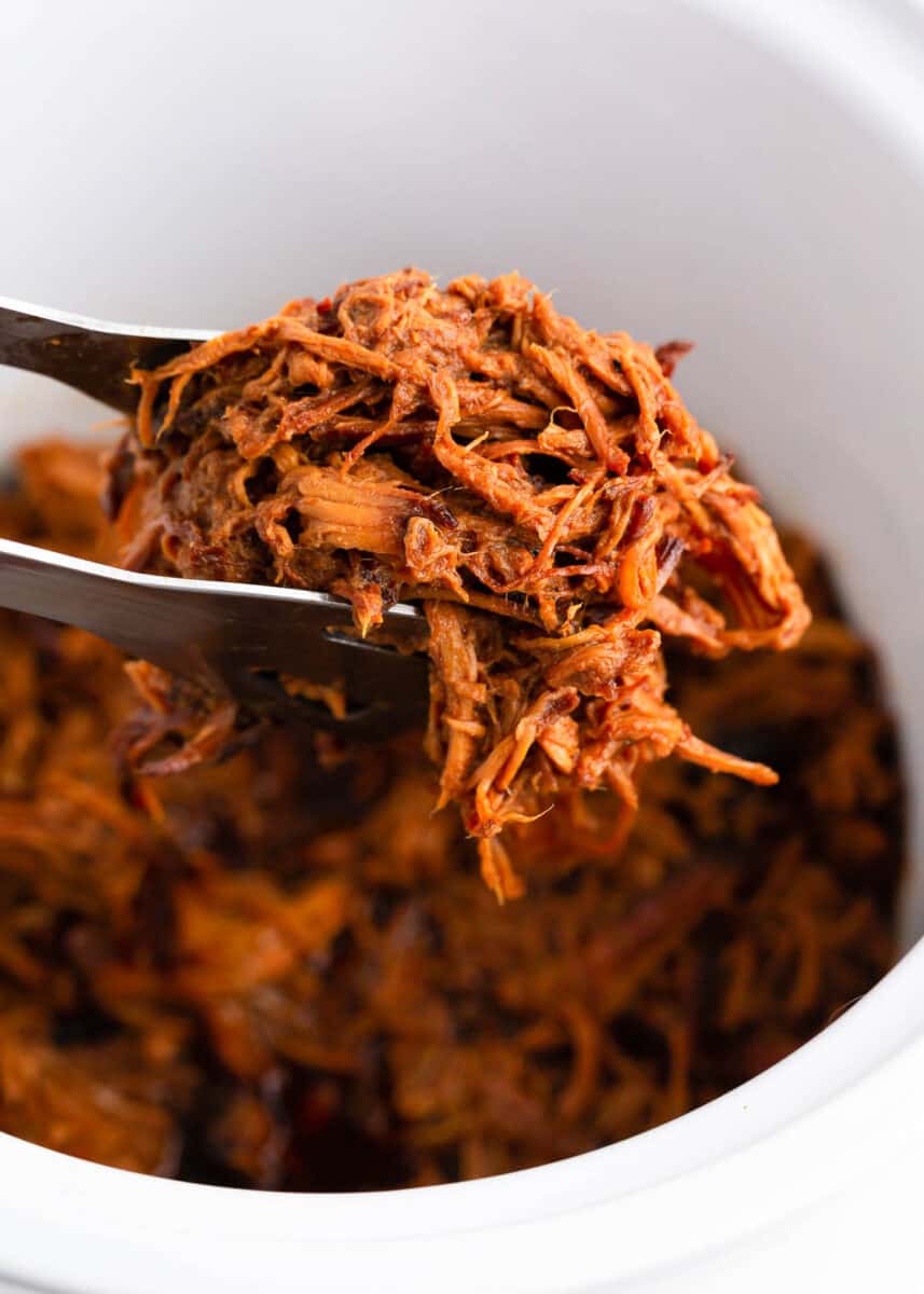 Lifting out honey chicken with tongs from crockpot.