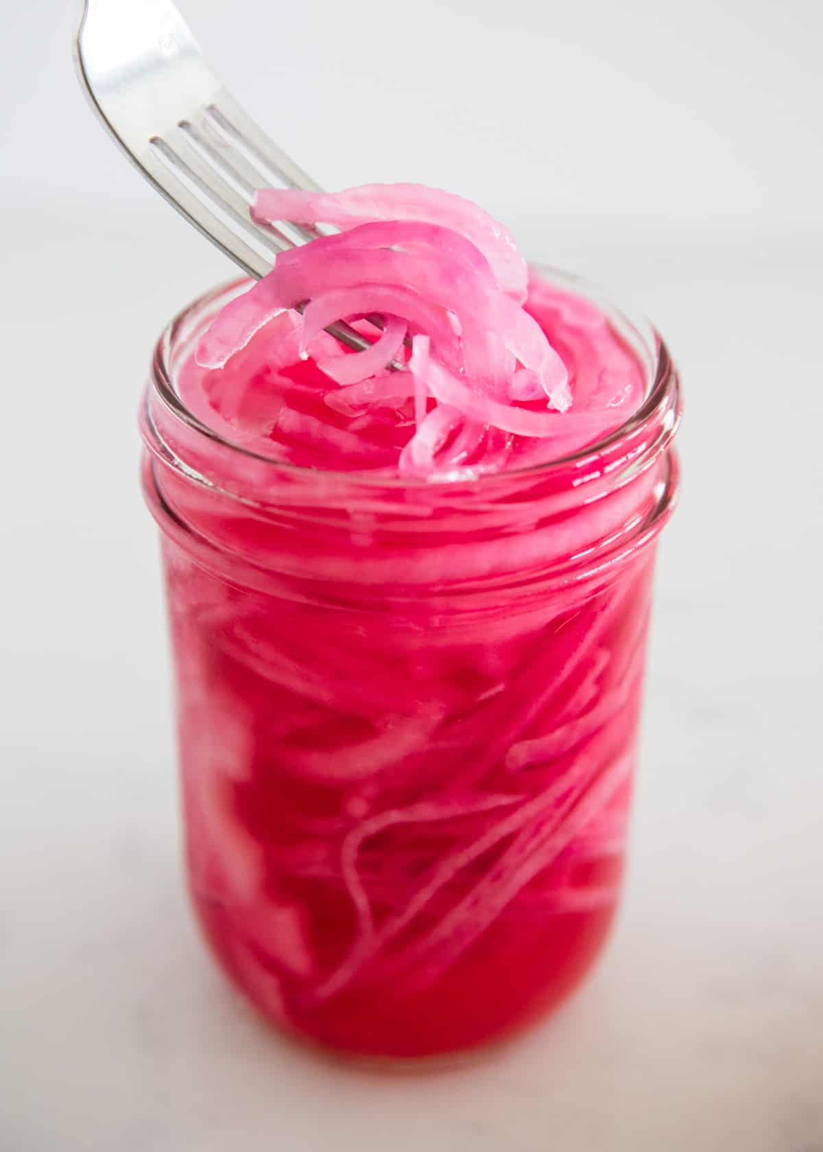 Lifting pickled red onions out of jar with a fork.