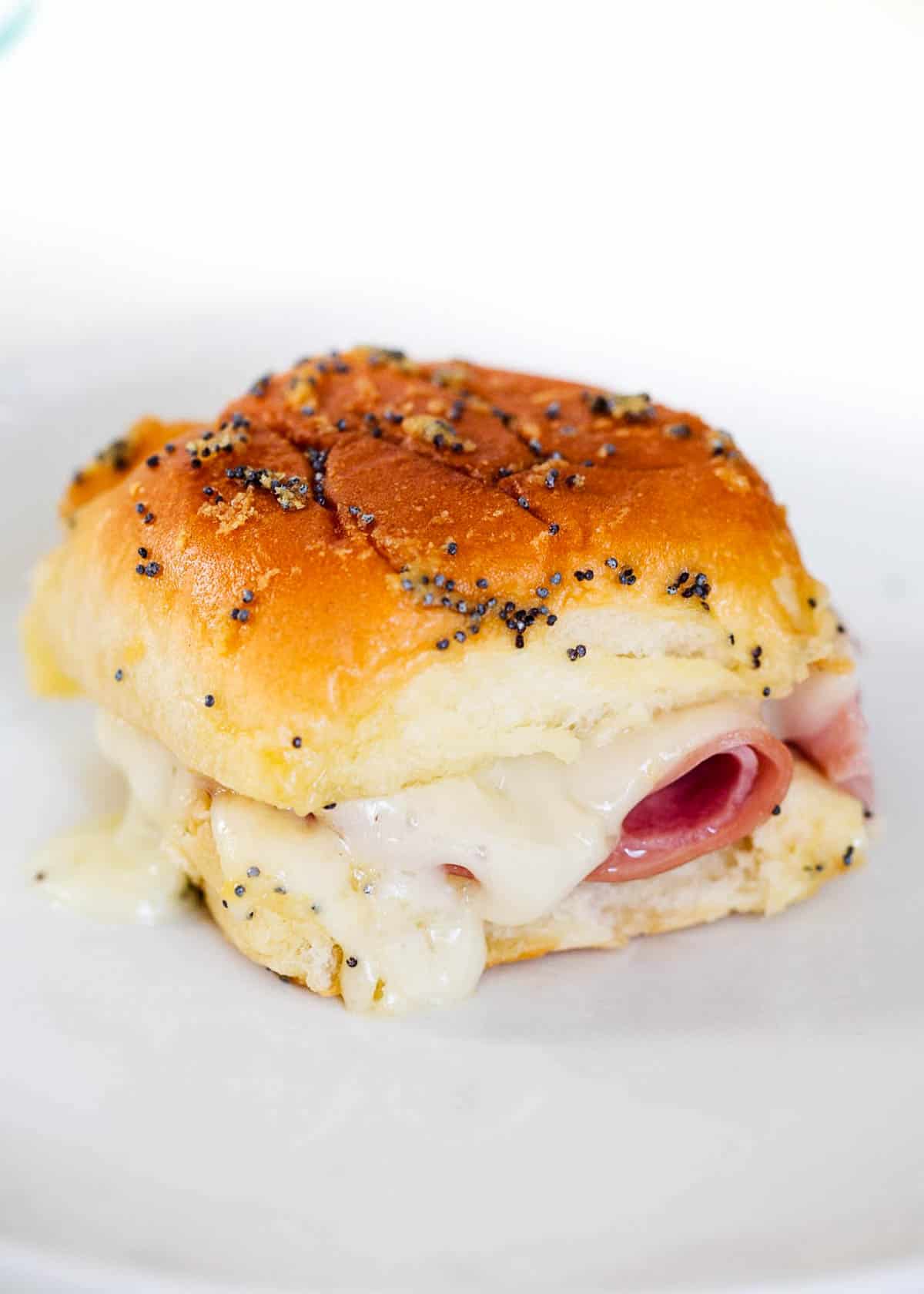 These easy ham and cheese sliders with poppy seed sauce are the perfect appetizer or main dish recipe for game day, parties or the holidays. The best way to use up any leftover ham! A baked ham and cheese slider on a plate.