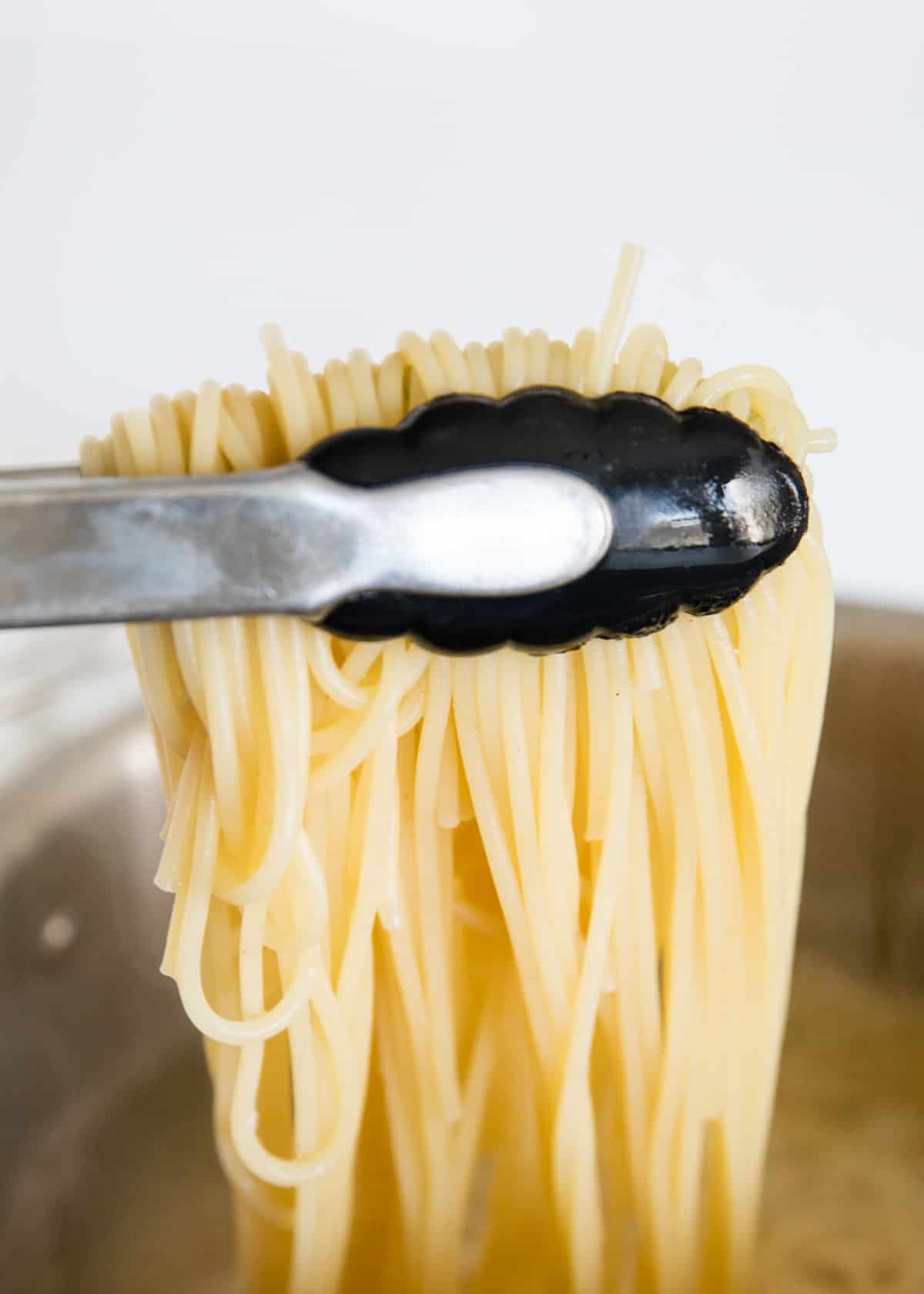 Lifting pasta out of the pot with tongs.