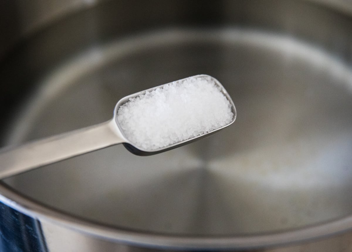 Spooning salt into a pot of water.
