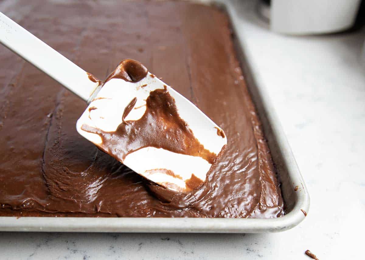 Spreading chocolate frosting on top of Texas sheet cake with spatula.