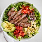 steak salad with avocado in white bowl