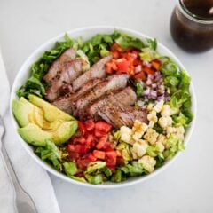 Grilled steak salad with avocado in a white bowl.