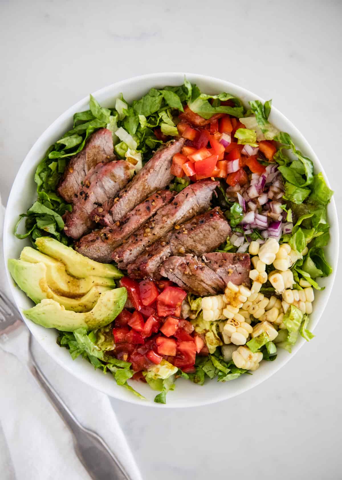 Steak salad with avocado in a white bowl.