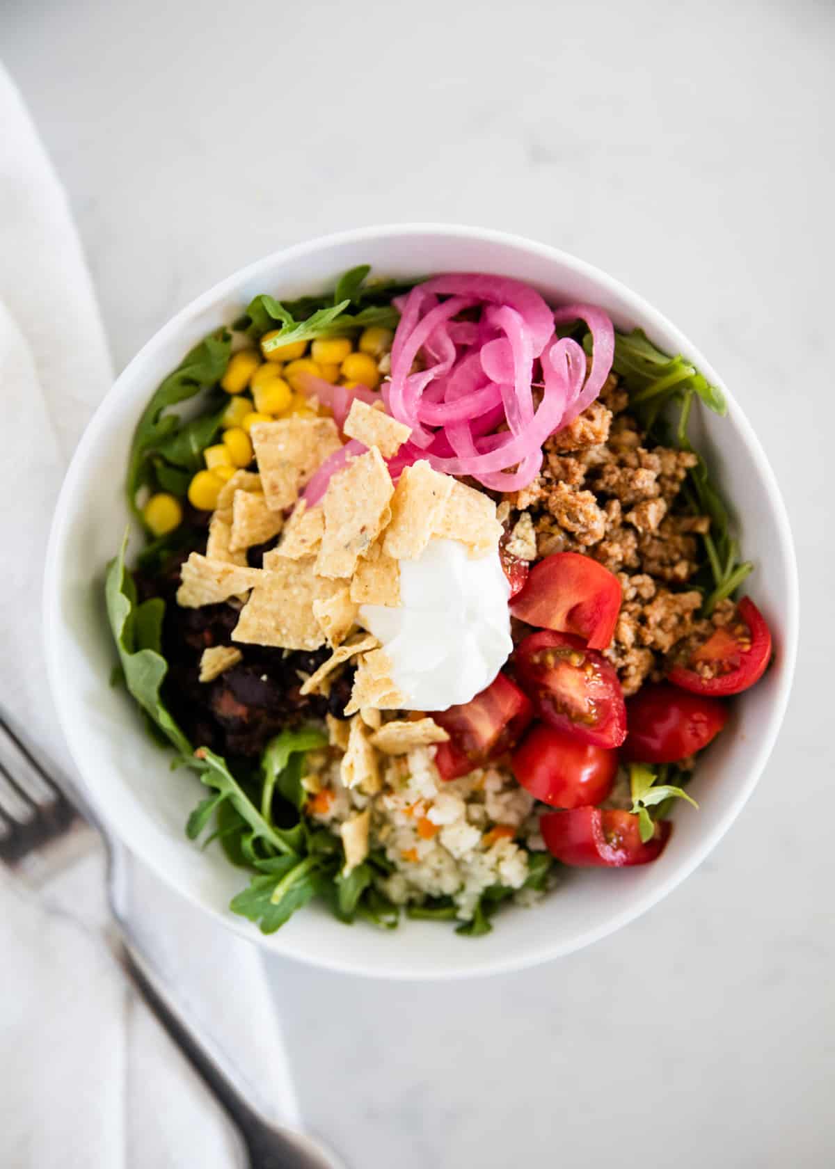 Taco salad with pickled onions in white bowl.