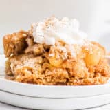 Apple dump cake with whipped cream on a white plate.