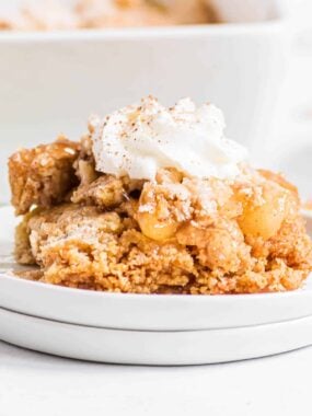 Apple dump cake with whipped cream on a white plate.