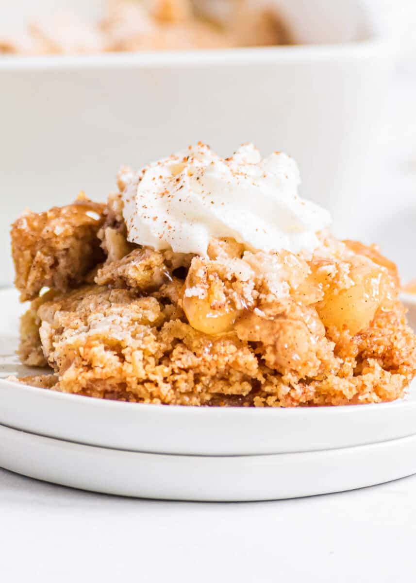 Apple dump cake with whipped cream on a white plate.