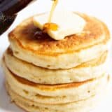 Pouring syrup on a stack of buttermilk pancakes.