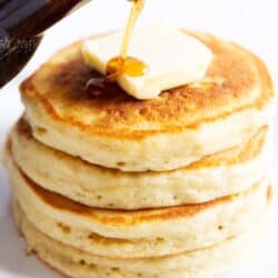 Pouring syrup on a stack of buttermilk pancakes.