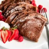 The best chocolate crepes on a white plate with strawberries.
