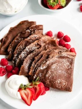 Folded chocolate crepes on a plate.