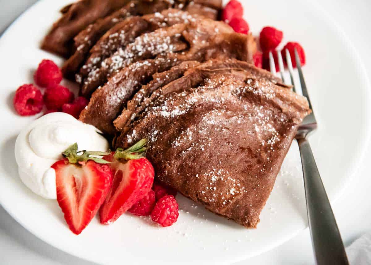 The best chocolate crepes on a white plate with strawberries.