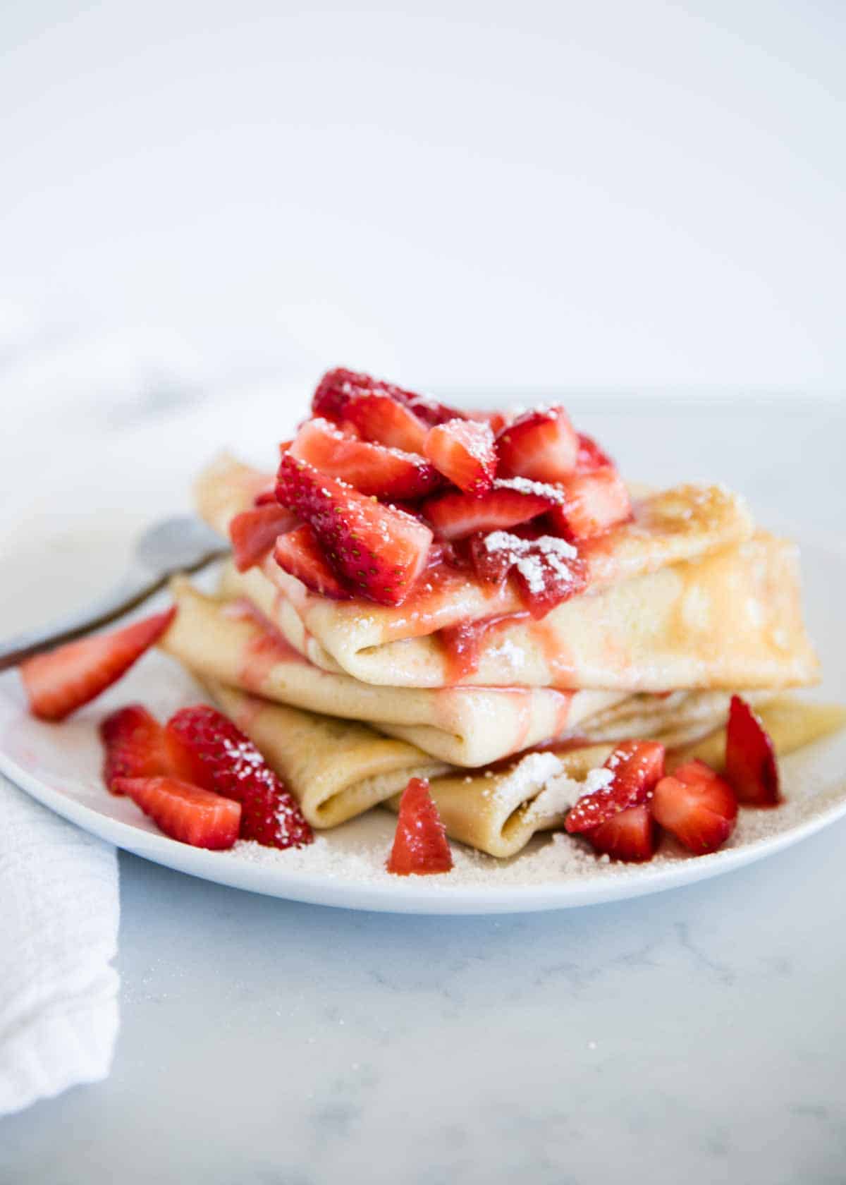 Homemade strawberry crepes in just 15 minutes! Fill them with a sweet cream cheese filling and fresh strawberry sauce. These make the perfect easy breakfast or dessert! Stack of strawberry crepes.