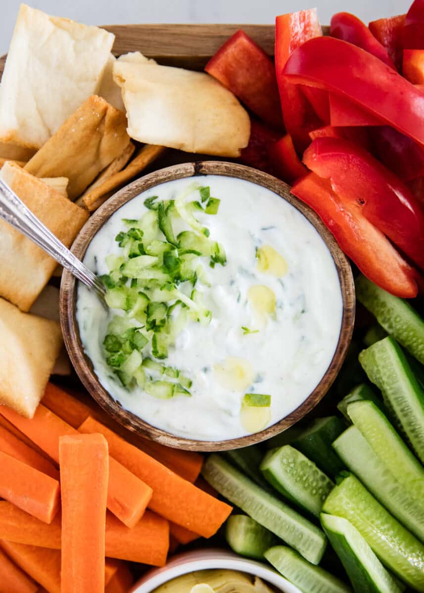 Tzatziki sauce in wooden bowl with vegetables.