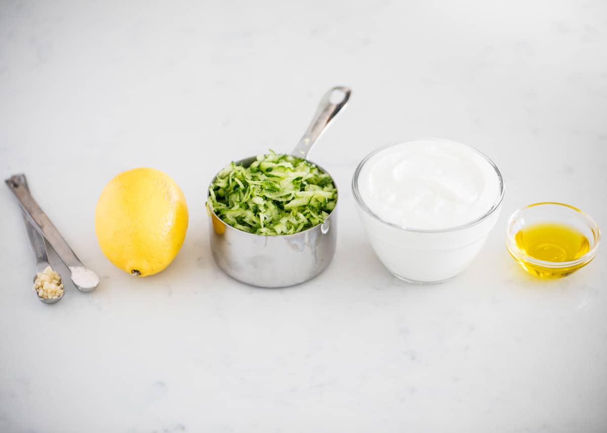 Tzatziki sauce ingredients on marble counter.