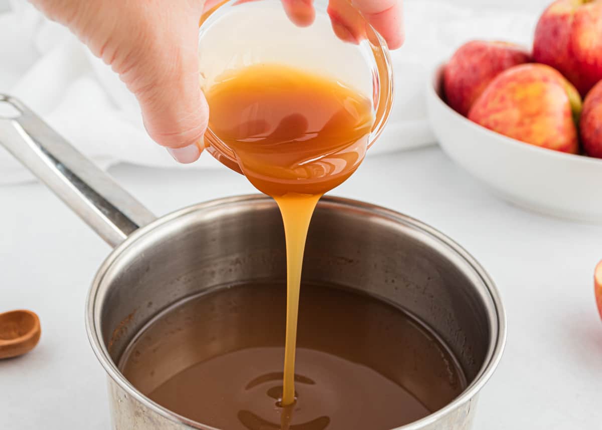 Pouring caramel into pot of apple cider.