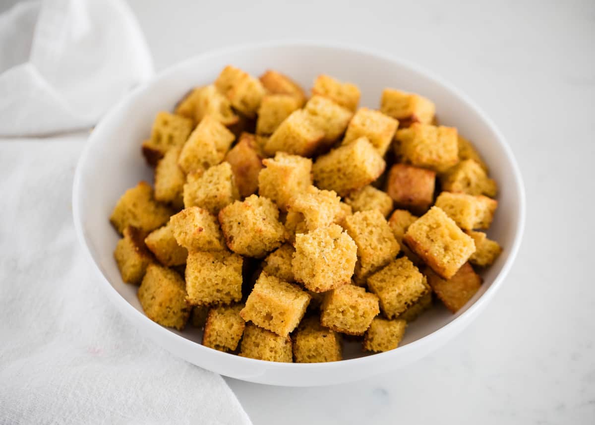 Cornbread croutons are so easy to make and are the perfect way to use up leftover cornbread. Elevate your salads in the most simple and delicious way! Cornbread croutons in a white bowl on the counter.