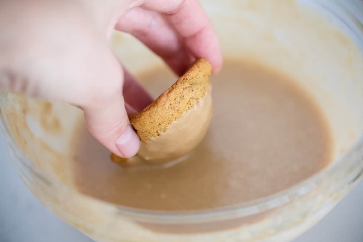 Dipping a soft pumpkin cookie halfway into the bowl of homemade caramel icing for a sweet frosted finish.