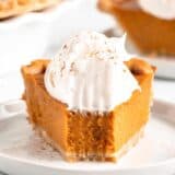 pumpkin pie with whipped cream on white plate with
