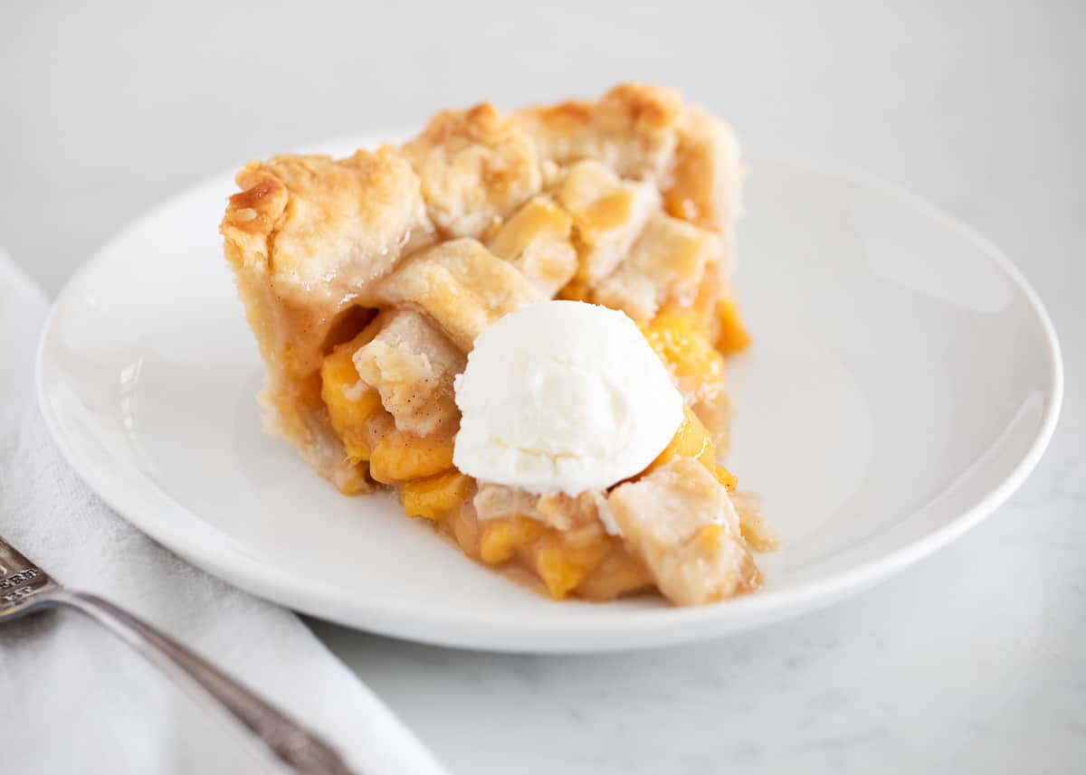Learn to make the best peach pie with the option of a double crust or single with a crumble topping. A homemade (or store-bought) buttery flaky golden crust filled with a fresh peach filling is the perfect summer dessert! Sliced peach pie on plate.