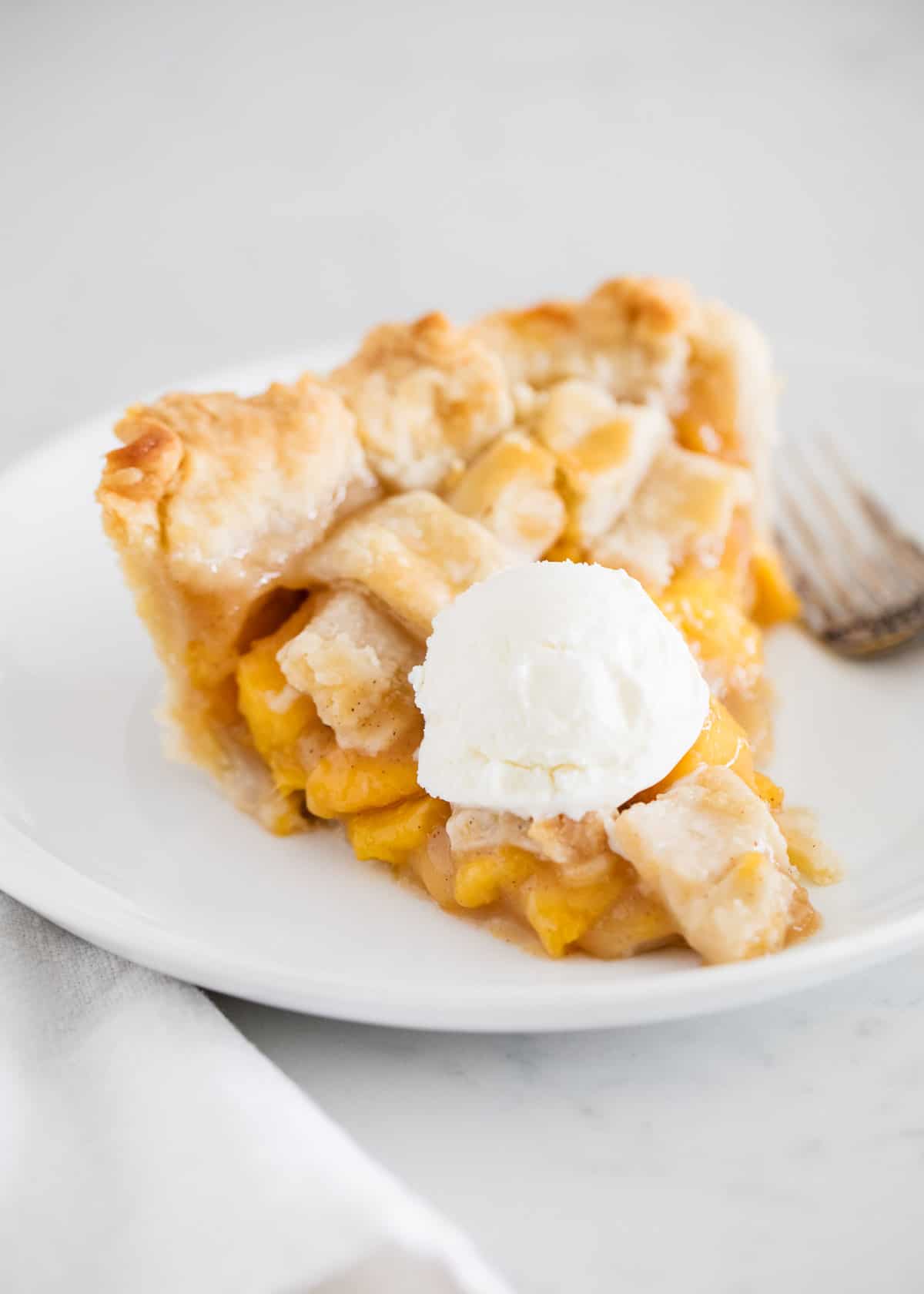 Slice of peach pie with ice cream.