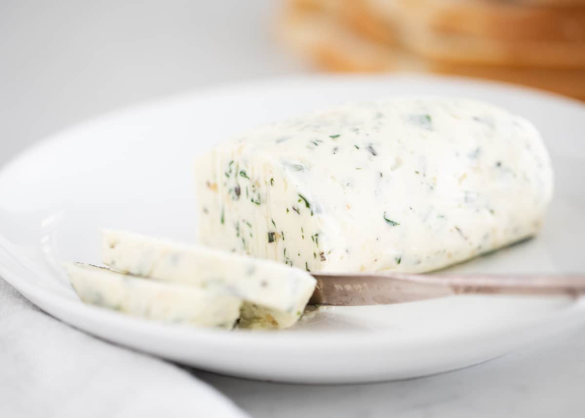 Elevate your dish with this flavorful garlic herb butter. Prepped in just 10 minutes with 5 simple ingredients. Great for adding to meat, bread, vegetables and more. Garlic herb butter sliced on plate.